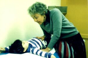 Remembering Dr. Audrey Evans. Older woman gently examining a child lying on a medical table.