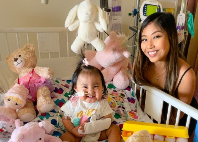 Smiling little girl in hospital bed and woman smiling next to the bed.