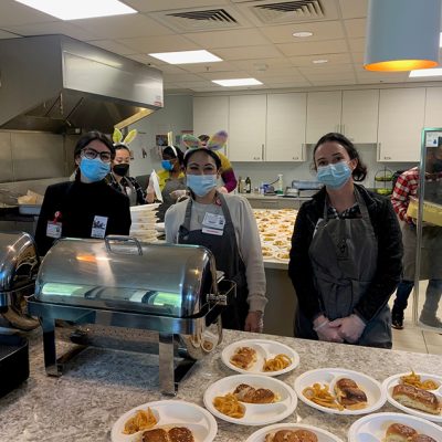Corporate Meal Group Corporate Meal Group: A megaBITES corporate meal group serving lunch to families. Group of volunteers in aprons and masks serving plates of food in the Ronald McDonald House kitchen.