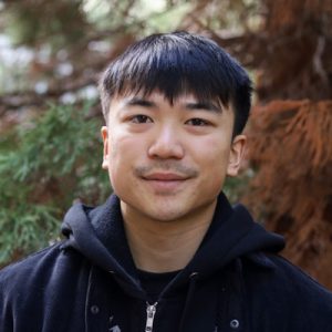 Darien Chung Headshot: Smiling man in a black hoodie sweater standing against a light background.