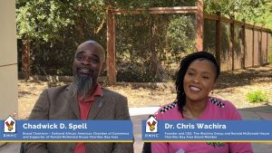 Chadwick D. Spell and Dr. Chris Wachira smiling while seated outdoors, with RMHC name tags and roles displayed at the bottom of the image.