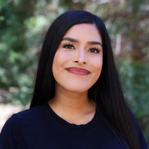 Headshot of Elena Lopez. Woman smiling with greenery in the background.
