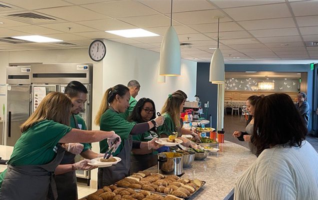 Enterprise megaBITES megaBITES group, Enterprise, in green shirts and aprons serve hot meals to guests in the Ronald McDonald House kitchen.