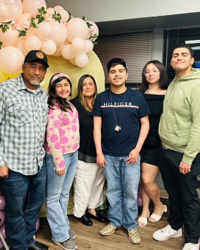 The Medina Flores family smiling together indoors in front of a pink balloon arch.