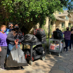 Izzy's family dropping off donations in memory of her birthday. Group of masked volunteers standing with carts full of donation bags and supplies outside a building.