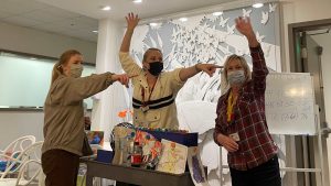 Three masked women enthusiastically pointing and leading an activity in a decorated indoor RMHC space.