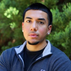Jonathan Cardenas 2025 400p Headshot of Jonathan Cardenas: Man wearing a sweater and leafy green background.
