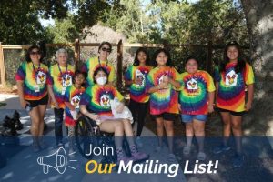 Group of RMHC families in tie-dye shirts smiling outdoors next to a graphic promoting the mailing list.
