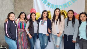 Mujeres Mejorando Vidas staff. Seven women standing together in front of birthday decorations and balloons.