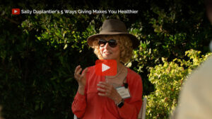 Gerontologist and Founder, Sally Duplantier. Sally Duplantier wearing sunglasses and a hat, speaking outdoors in a video about the health benefits of giving.