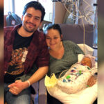 Jordan, Kristin, CeCe. Man and woman smile next to their newborn baby wrapped in a blanket and connected to medical tubes.