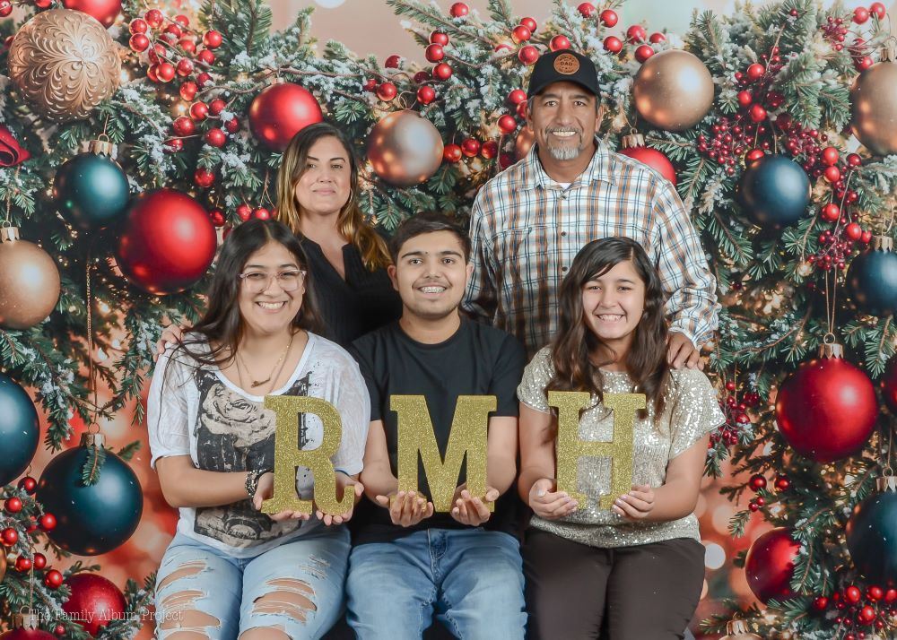 A group of people holding RMH Letters and smiling. There's a festive holiday backdrop behind.