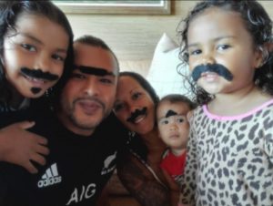 Smiling family of five, including children, wears fake mustaches and eyebrows while posing for a playful group photo indoors.