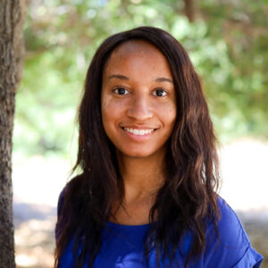 Sydney Morris, FSS. Woman in a blue blouse smiles while standing outside near trees.
