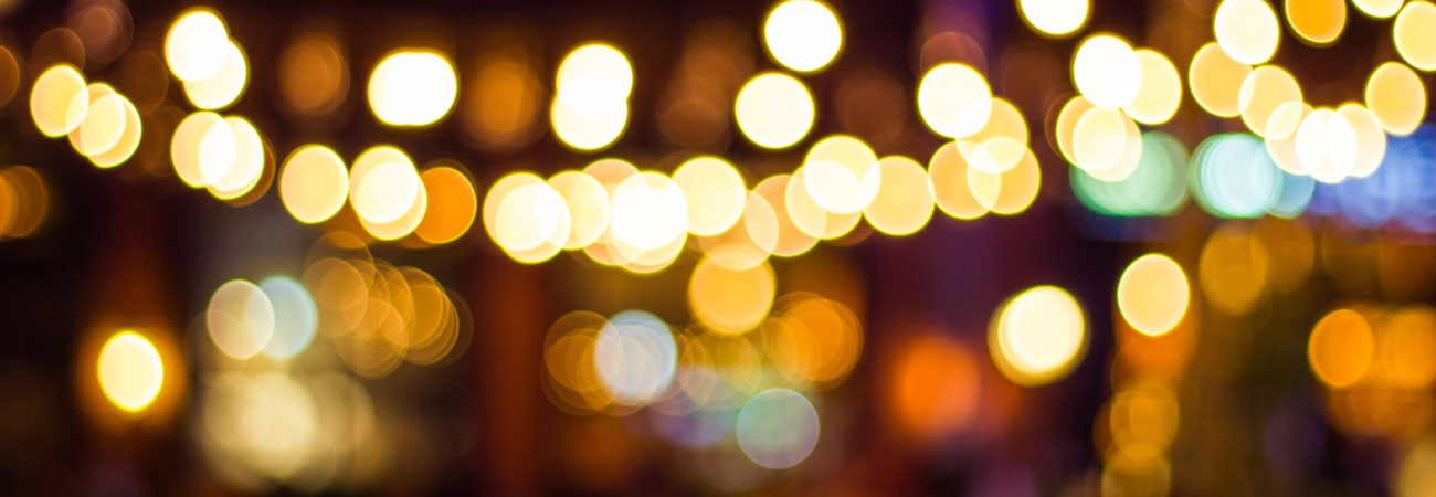 Defocused String Lights Background Blurred image of warm string lights glowing against a dark background, creating a bokeh effect.