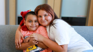 Benjamin and Trinity Franco. Two smiling children hugging closely on a couch, with a red teddy bear on the boy’s shoulder.