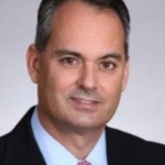 Headshot of board member Willie Hernandez, wearing a suit and smiling