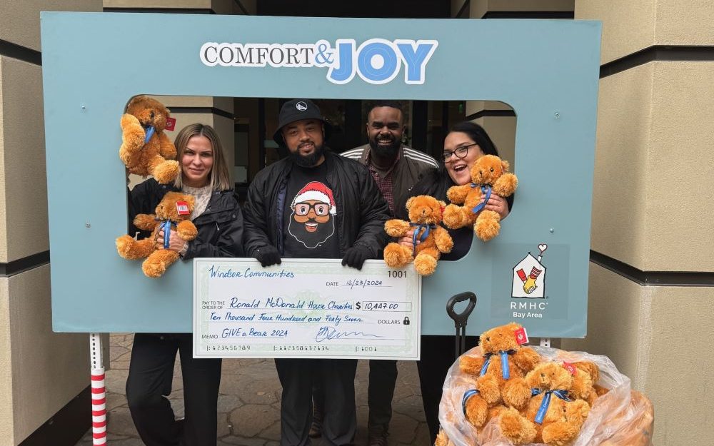 Windsor Fundraiser Windsor Funraiser 2024: A group of four people smiling and holding brown teddy bears. There is a sign reading Comfort & Joy in front of them.