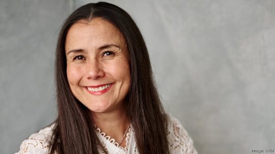 Image of a woman smiling with a grey background.