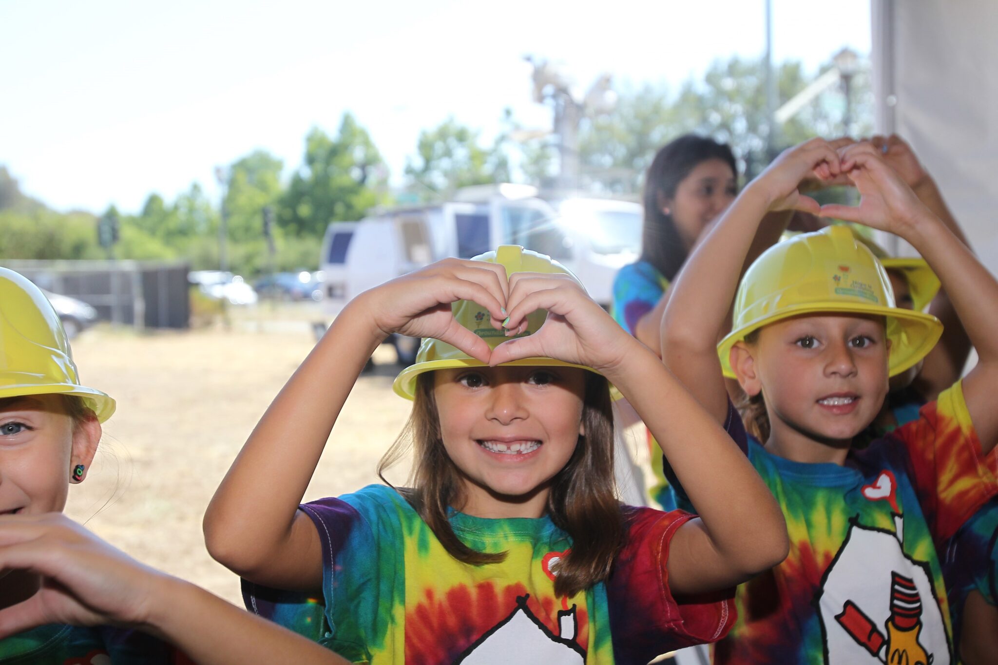 Kids making hearts with their hands wearing tie-dye shirts and hard hats.