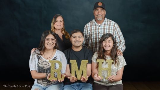 The Medina Flores family poses for a portrait holding gold glitter letters spelling RMH, as part of The Family Album Project.