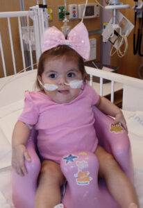 Baby Miracle. Baby girl with nasal tubes and a big pink bow sitting in a hospital room baby chair.